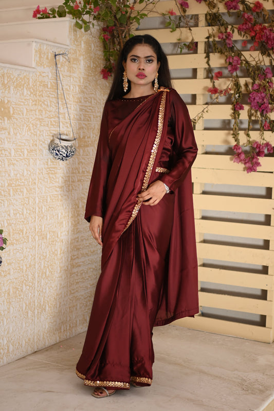 Woman wearing a maroon Silk saree 
outfit with gold trim in a decorated room.